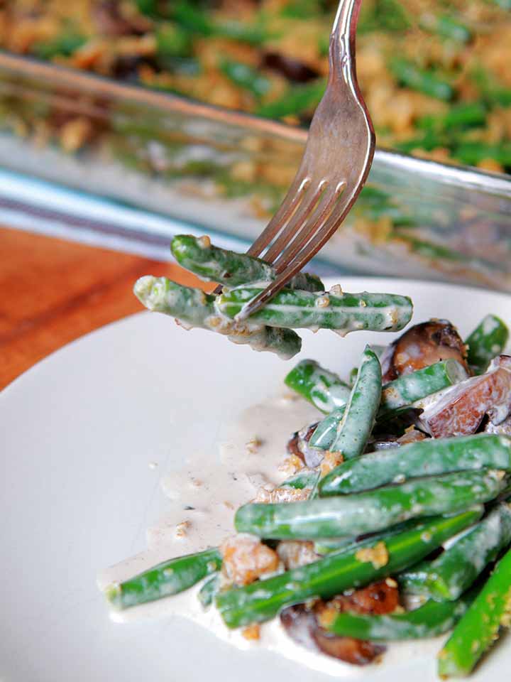A fork holds green beans over a plate of low calorie green bean casserole