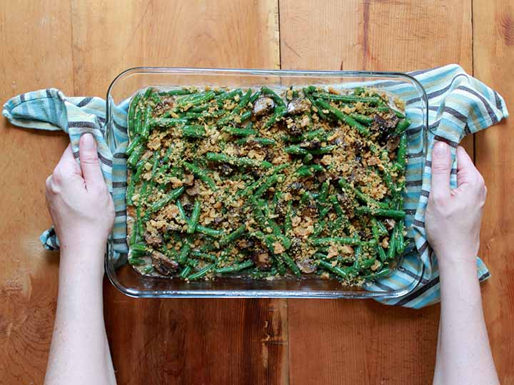 top down view of two hands holing a casserole dish filled with green beans, cream of mushroom sauce and crushed pork rinds