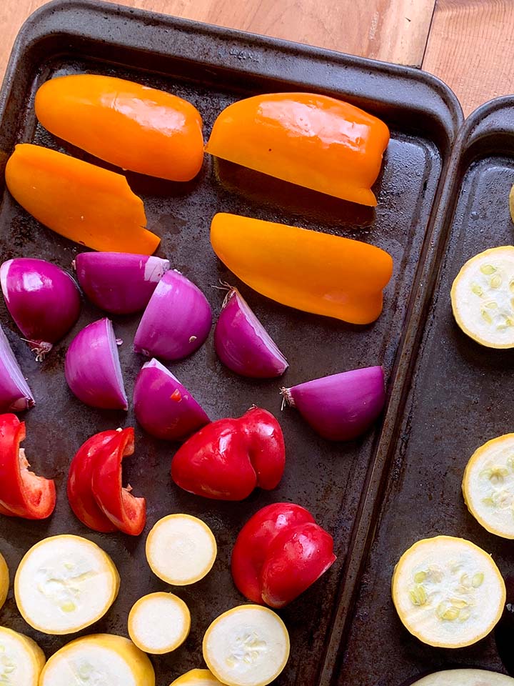 cookie sheets holding sliced eggplant, bell peppers, onions, yellow quash and yellow squash