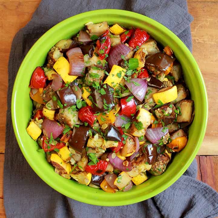 a top down image of a green bowl full of Keto ratatouille against a dark gray napkin