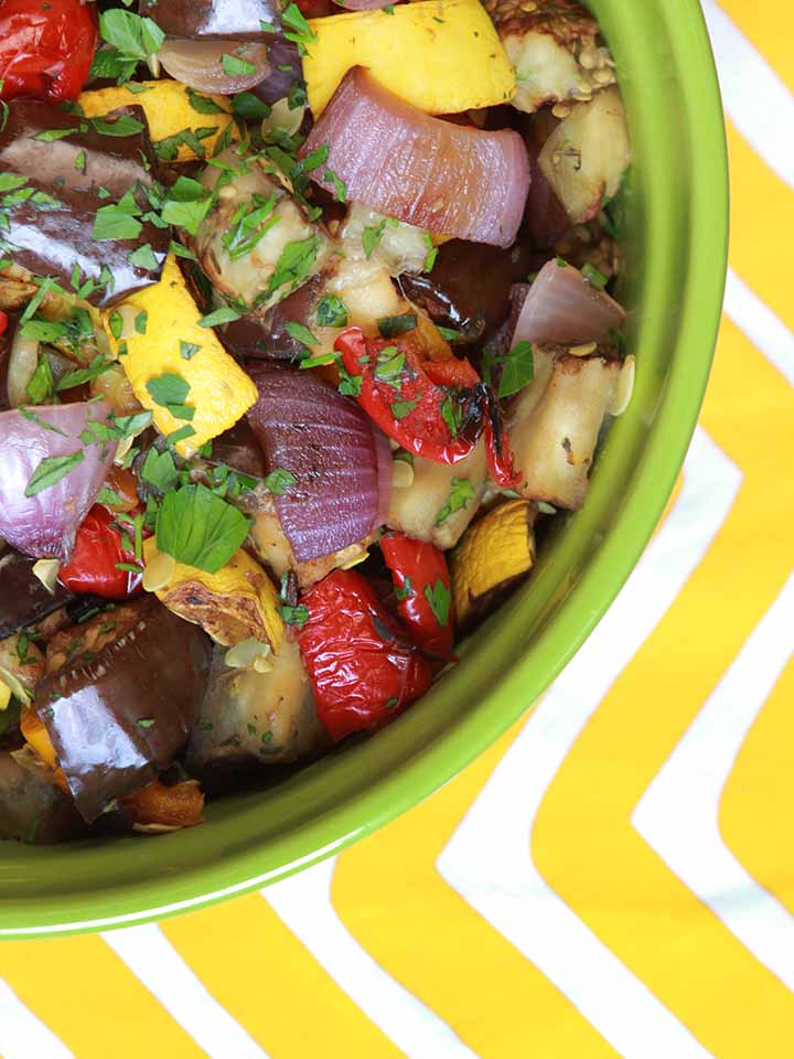 a green bowl of Vegan Ratatouille against a white and yellow patterned cloth