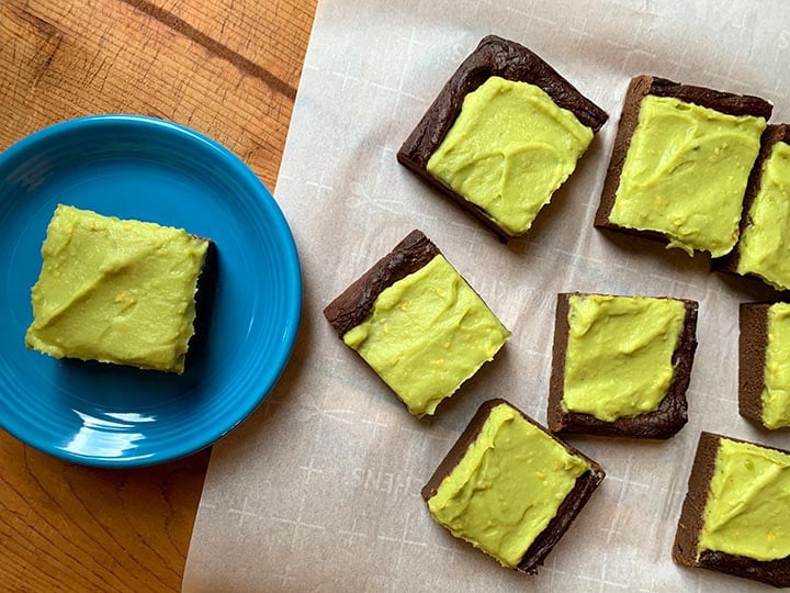 a top down view of a keto avocado brownie on a blue plate and 5 brownies on white parchment paper