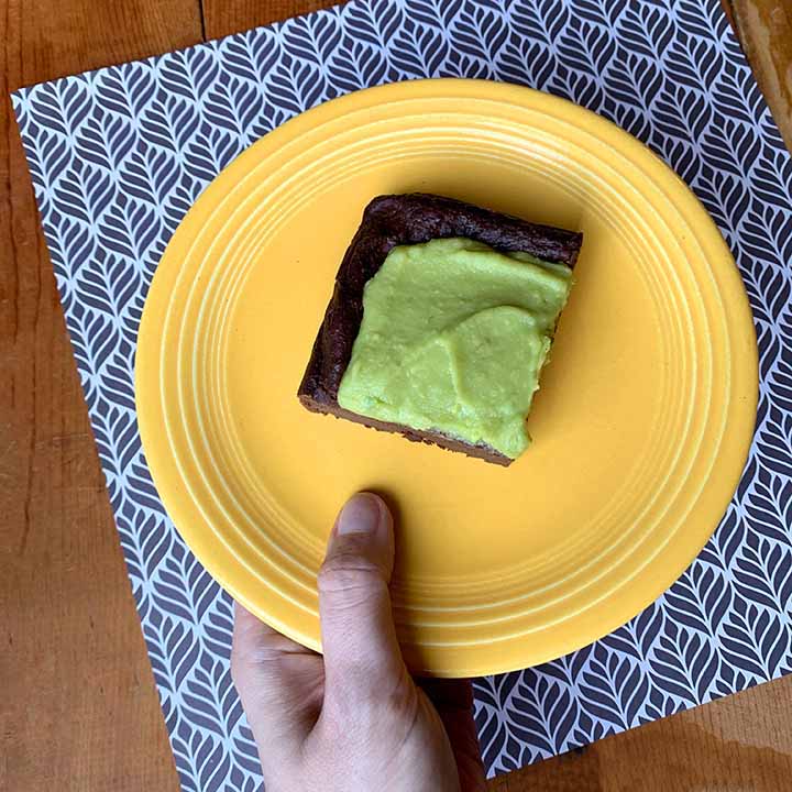 a hand holds a yellow plate with a gluten free dairy free avocado brownie