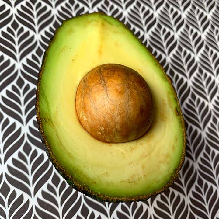 a half of a Hass avocado against a black and white patterned background