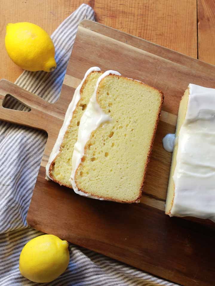 a top down view of low carb lemon pound cake on a cutting boards with some lemons strewn about