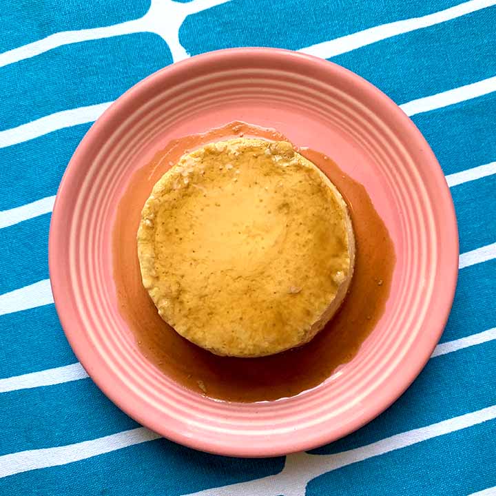 top down image of a piece of Keto creme caramel on a pink plate against a blue patterned background