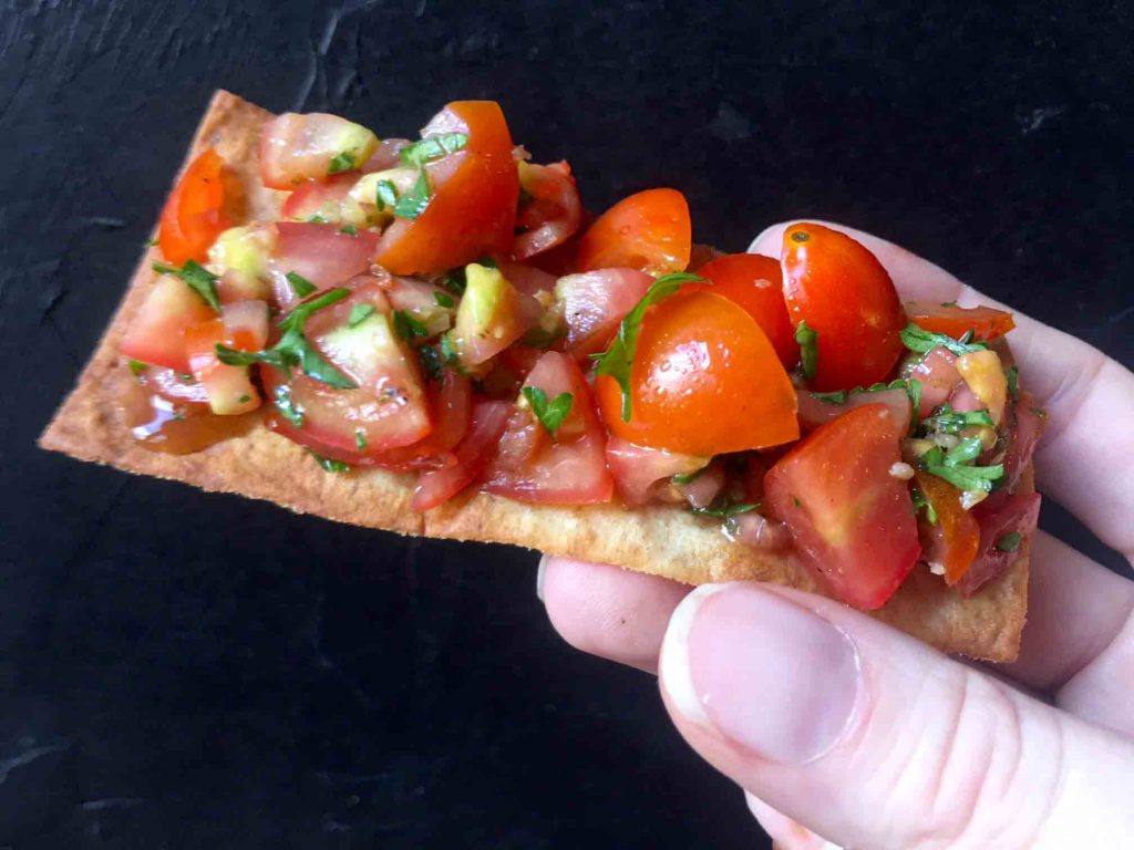 a hand holds a slice of Keto Bruschetta