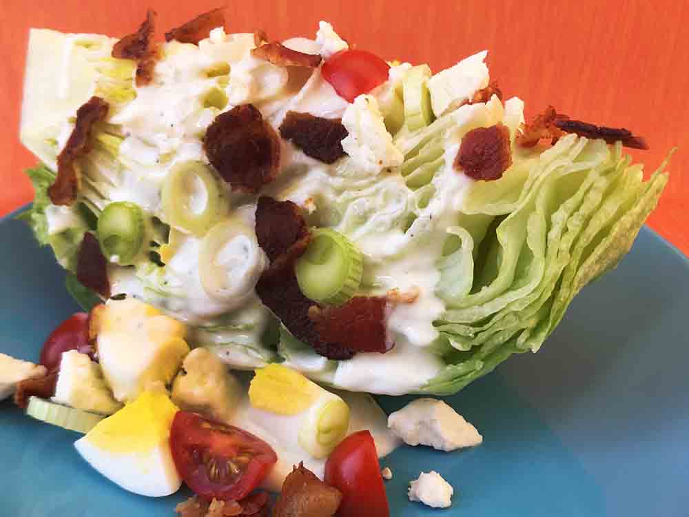 A Keto wedge salad on a blue plate against an orange background