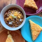 a top down view of a bowl of classic chili con carne and colorful plates of low carb cheesy jalapeno cornbread