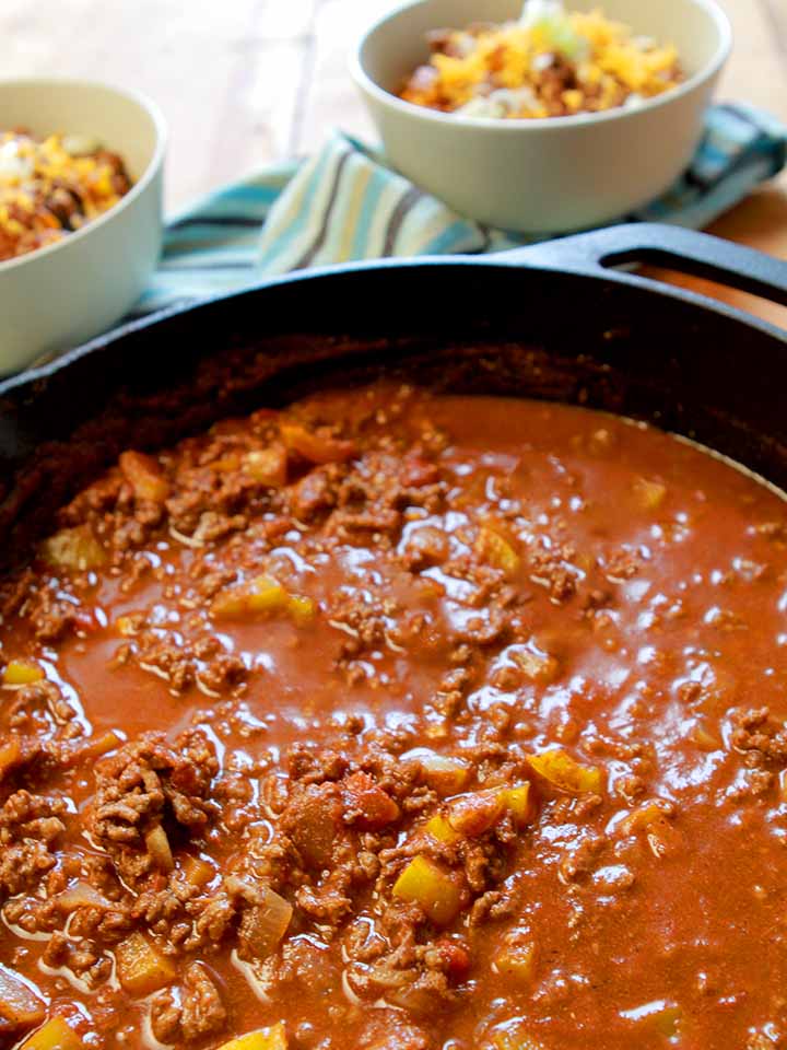 a cast iron pan holding easy chili con carne with bowls of the chili in the background