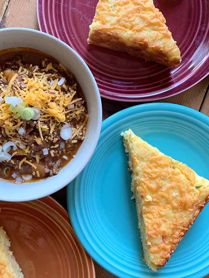 a top down view of a bowl of classic chili con carne and colorful plates of low carb cheesy jalapeno cornbread