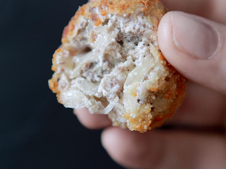 a hand holds a gluten free sauerkraut and sausage balls against a black background