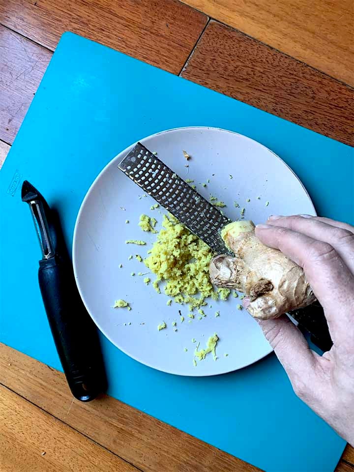 a hand grates a ginger root