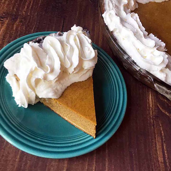 a slice of Keto pumpkin pie on a blue plate with a pumpkin pie in the background