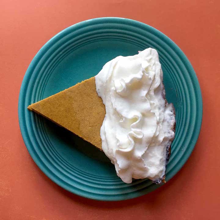 a slice of low carb pumpkin pie on a blue plate against an orange background