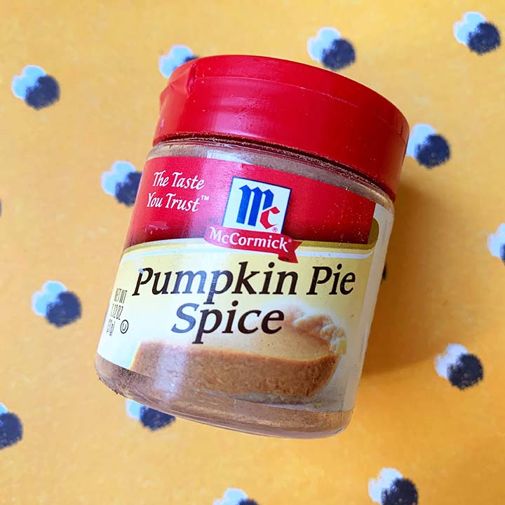 a container of pumpkin pie spice against a yellow patterned background