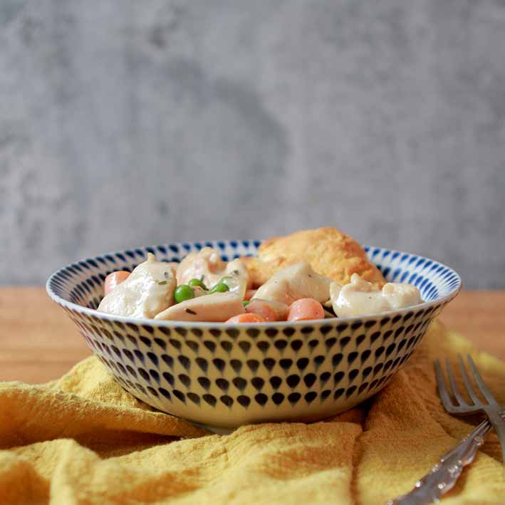 a side view of a bowl holding Keto chicken pot pie with a biscuit topping and a yellow napkin against a gray background