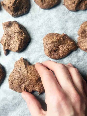 a hand picks up a Keto Chocolate Meringue Cookies