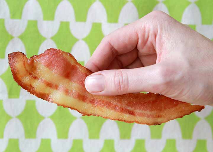 a hand holds a slice of Keto bacon