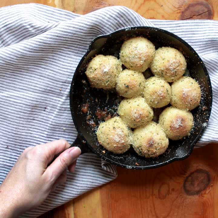 a hand holds a cast iron skillet with the rolls.