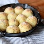A hand hold the handle of a cast iron pan full of Keto Garlic Bread Rolls
