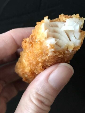 a hand holds a fish stick from fish and chips
