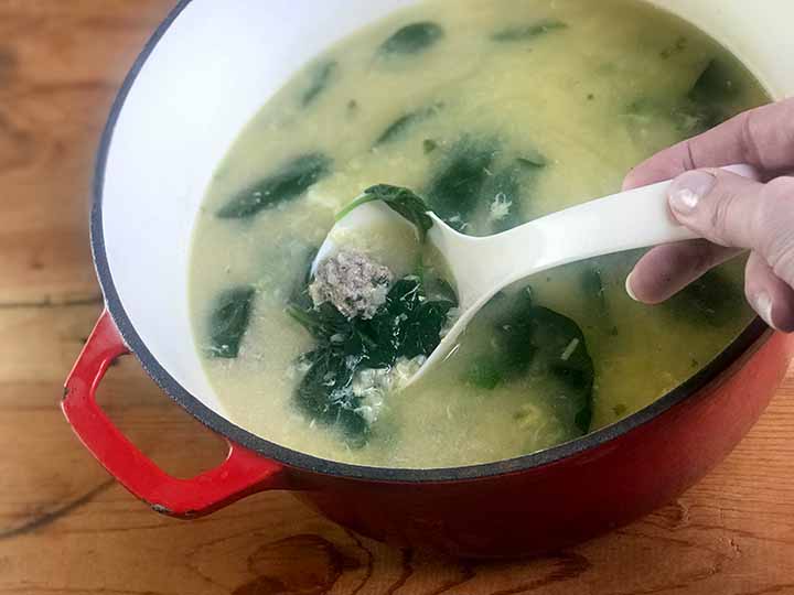 a hand is scooping up some low carb meatball soup from a red dutch oven