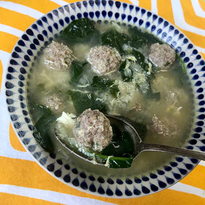 A bowl of low carb wedding soup with a spoon scooping up a bite