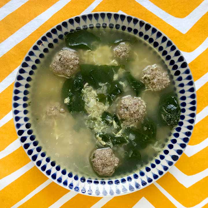 A bowl of Keto meatball soup against a brightly colored yellow background.