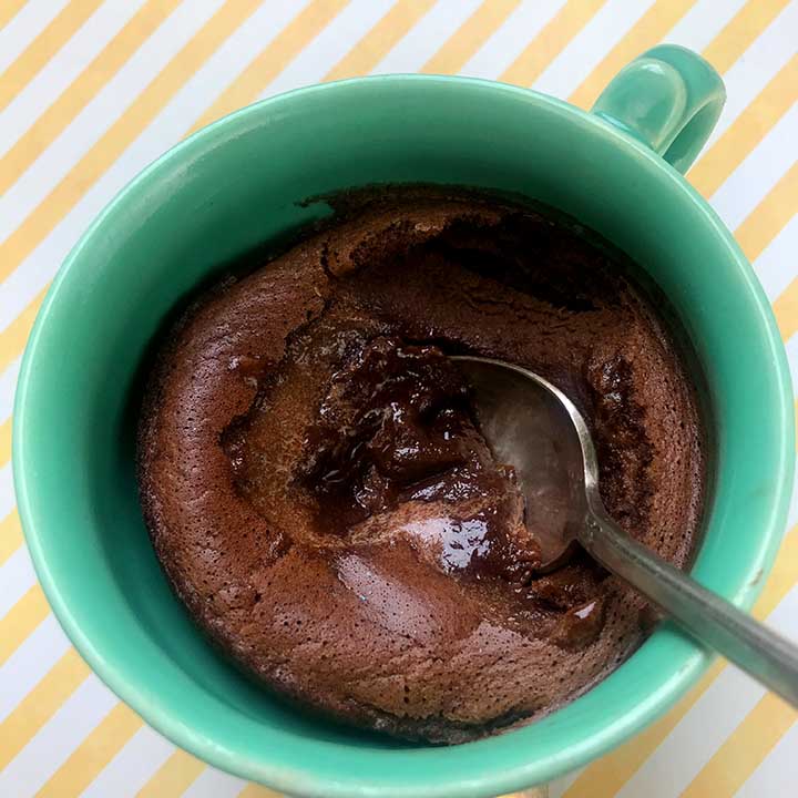 A low carb mug cake in a green cup against a yellow and white striped background