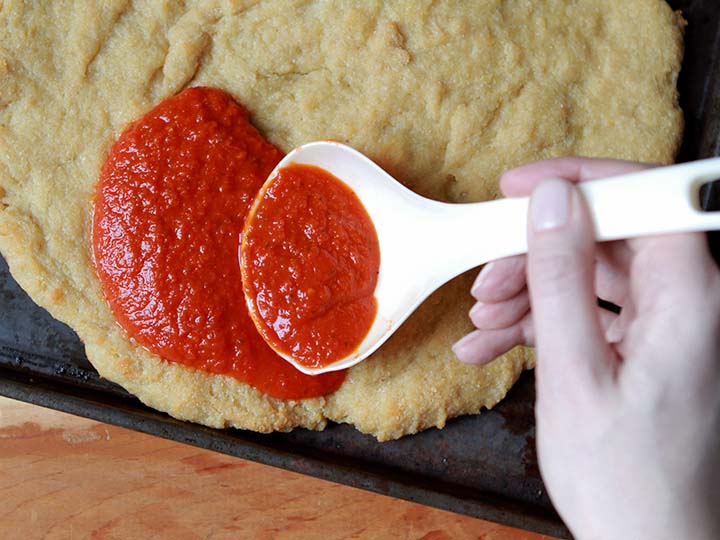 a hand puts sauce on a Yeast Dough Pizza Crust