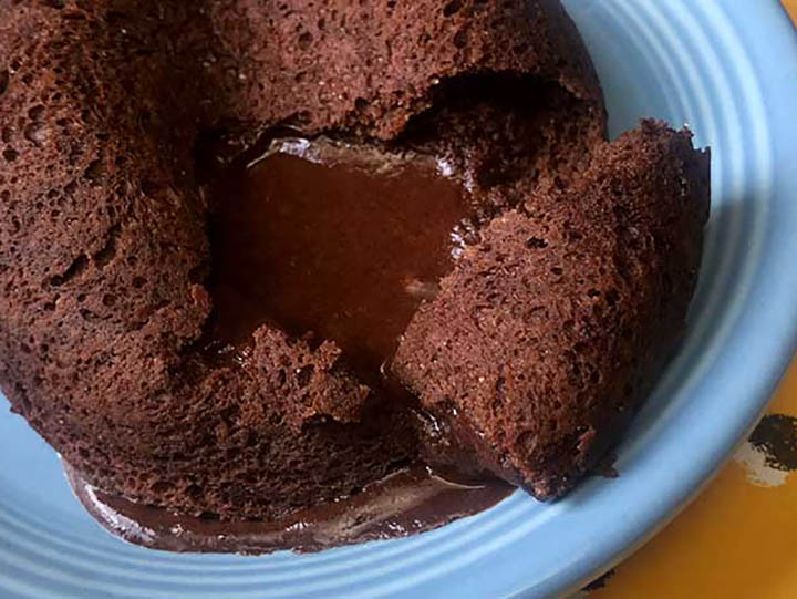 a low carb chocolate lava cake on a blue plate with inside chocolate goo coming out