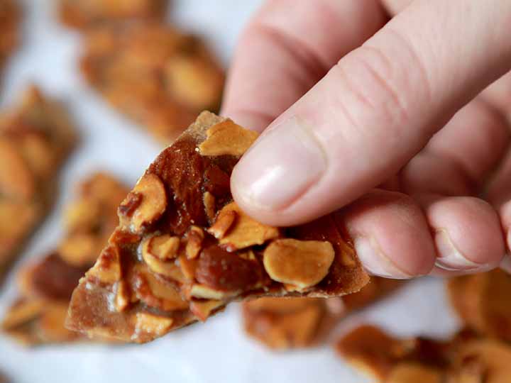 A hand holding a piece of low carb almond brittle bark