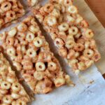 a top down close up view of 8 low carb keto cereal bars on white parchment paper against a wooden tabletop