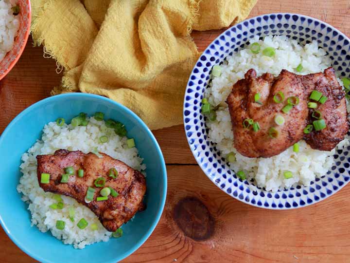 Two colorful bowls holding Keto chicken thighs on a bed of coconut cauliflower rice