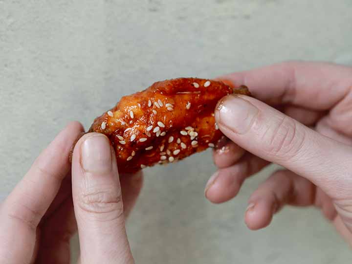 2 hands hold a healthy Korean BBQ Chicken Wing