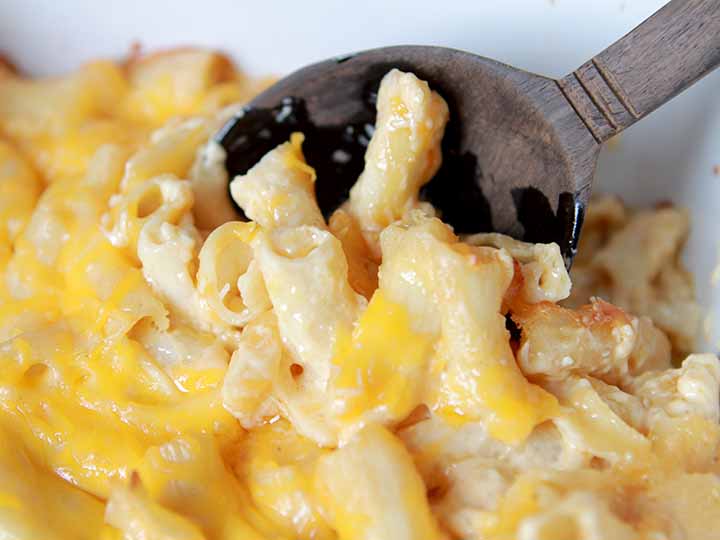 close up image of a brown wooden spoon dishing up healthy mac and cheese