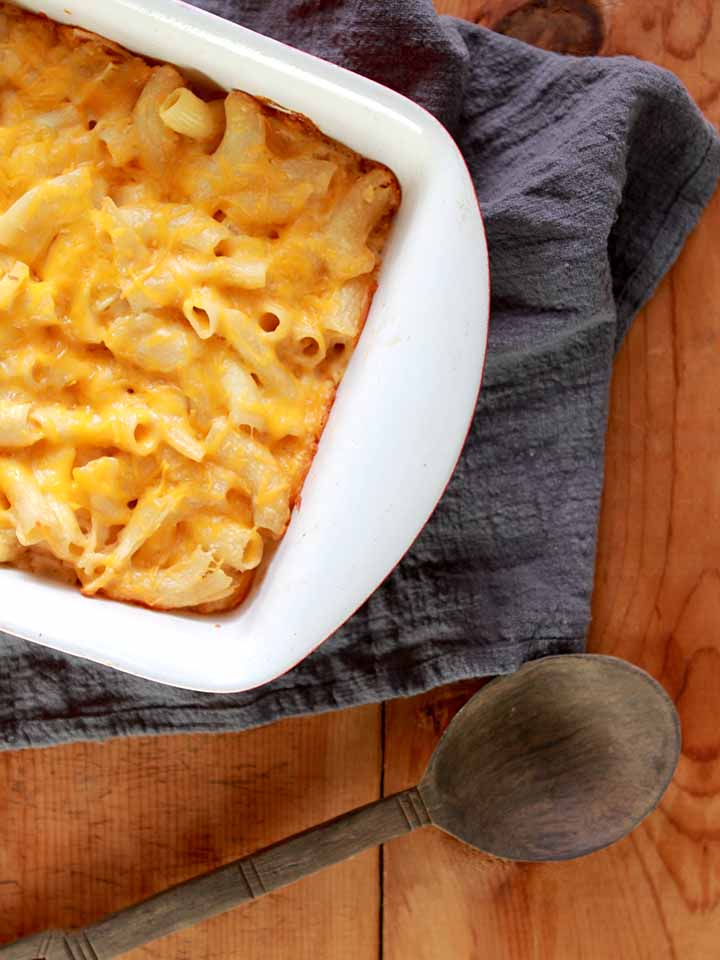 a white casserole dish of low carb macaroni and cheese on a gray cloth with a wooden spoon