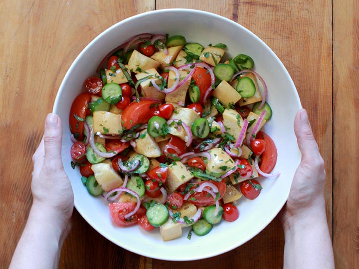 Two hands hold a big white bowl of Panzanella Italian Bread Salad