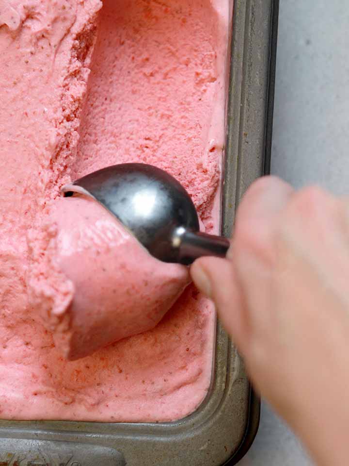 A hand scoops out healthy Ketogenic strawberry frozen yogurt