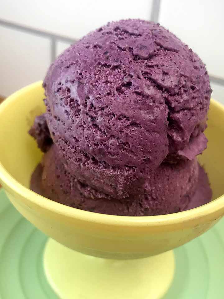 A yellow bowl holds 2 coops of Gluten Free Blueberry Ice Cream