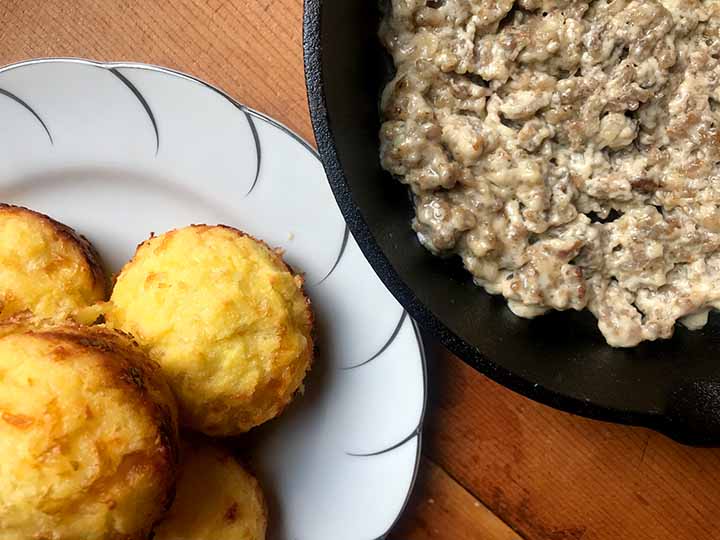 A white plate of low carb biscuit and a cast iron pan holding sausage cream gravy
