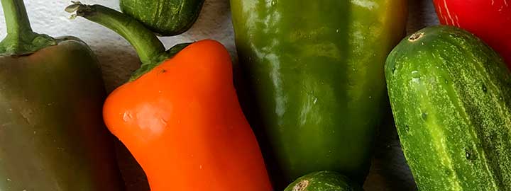close up image of cucumbers and red, orange and green bell peppers