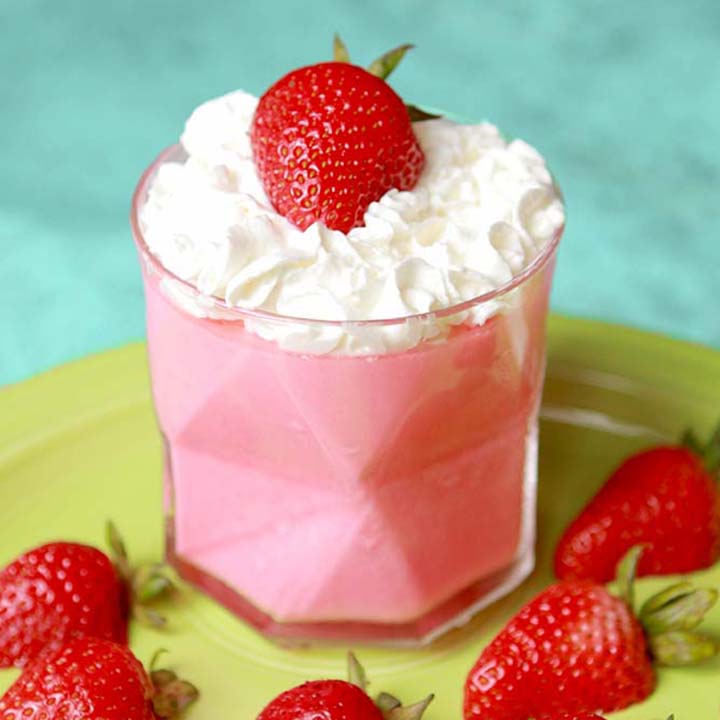 A glass of Strawberry Fluff Salad against a green plate with sliced strawberries on it