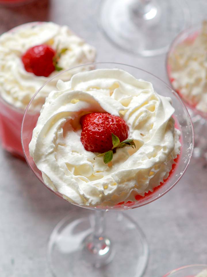 a martini glass holds a portion of Strawberry Fluff Salad with whipped cream and a strawberry on top
