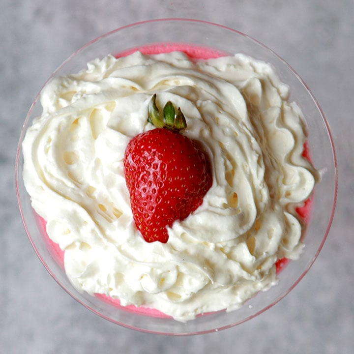 a martini glass holds a portion of sugar free Jello gelatin with whipped cream and a strawberry on top