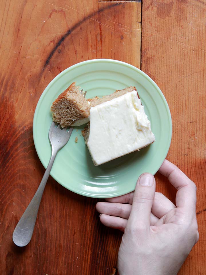 a hand holds a green plate of Holiday spice cake on a rough wooden tabletop