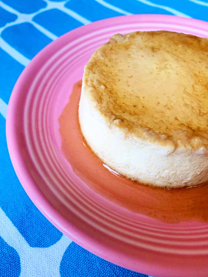 a side view of a piece of Keto creme caramel on a pink plate against a blue patterned background