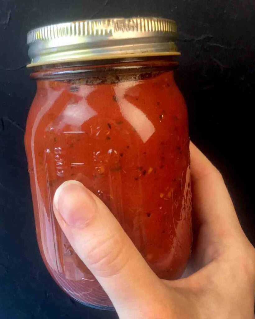 a hand holds a jar of sugar-free tomato sauce