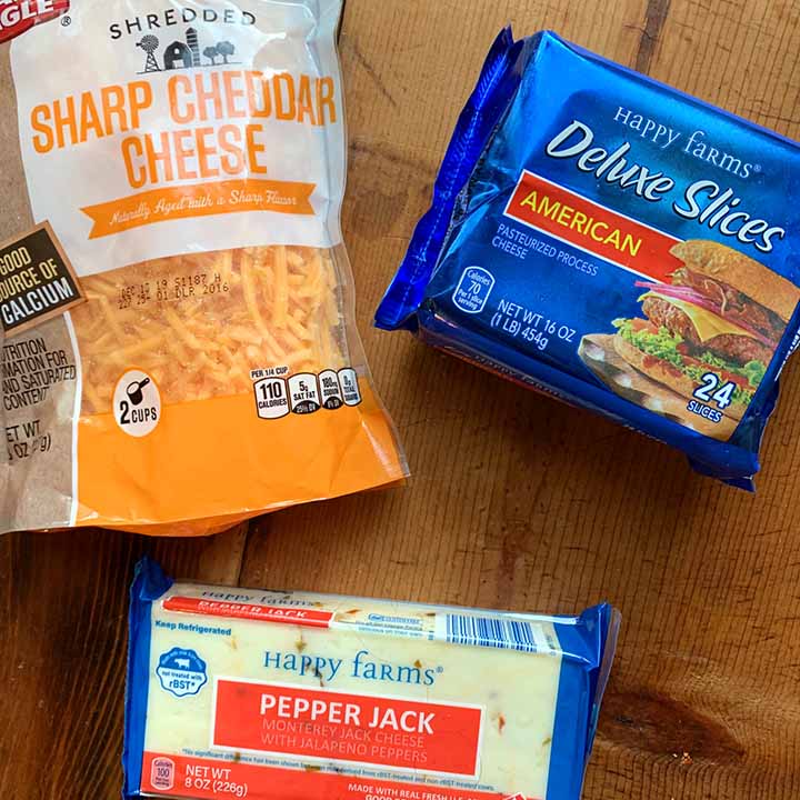 cheddar, colby jack and American cheese against a wooden tabletop